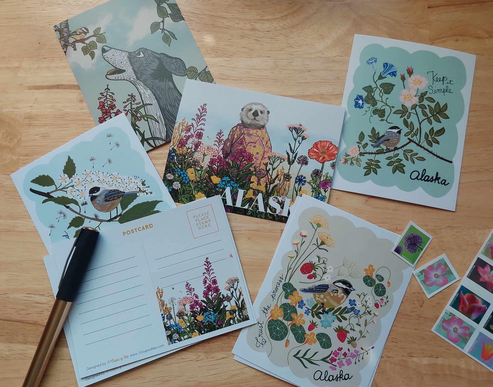 Collection of nature-themed cards and stickers on a wooden surface with a pen.